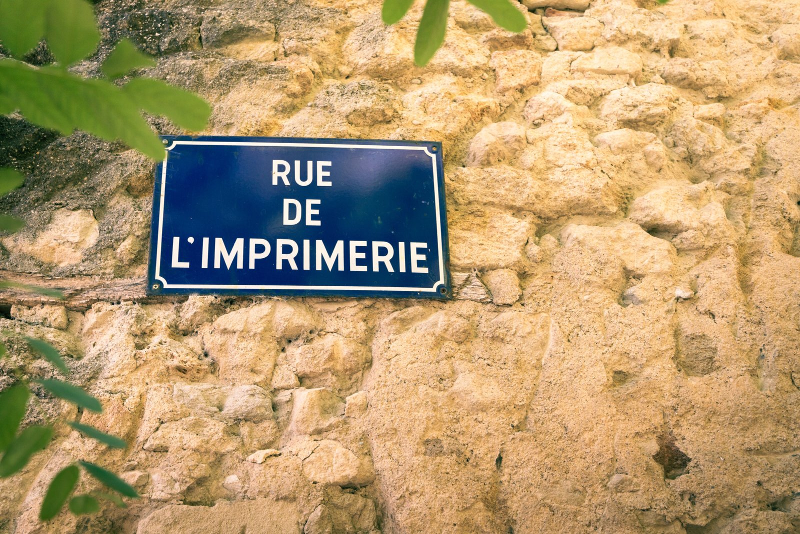 Panneau de rue sur un mu en pierre indiquant "Rue de l'imprimerie"