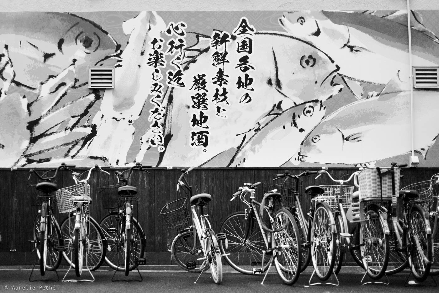 Une série de vélos devant un mur peint avec des poissons stylisés et du texte en japonais