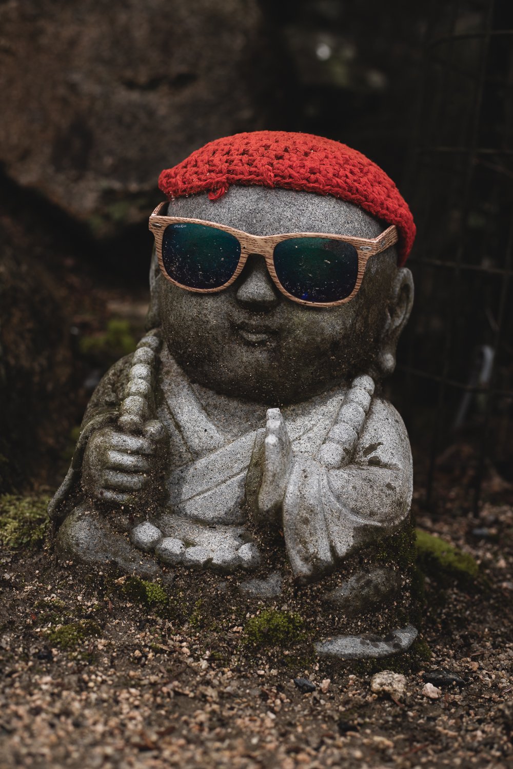 Au statuette aux allures de moine en pierre. Elle porte un bonnet rouge et des lunettes de soleil
