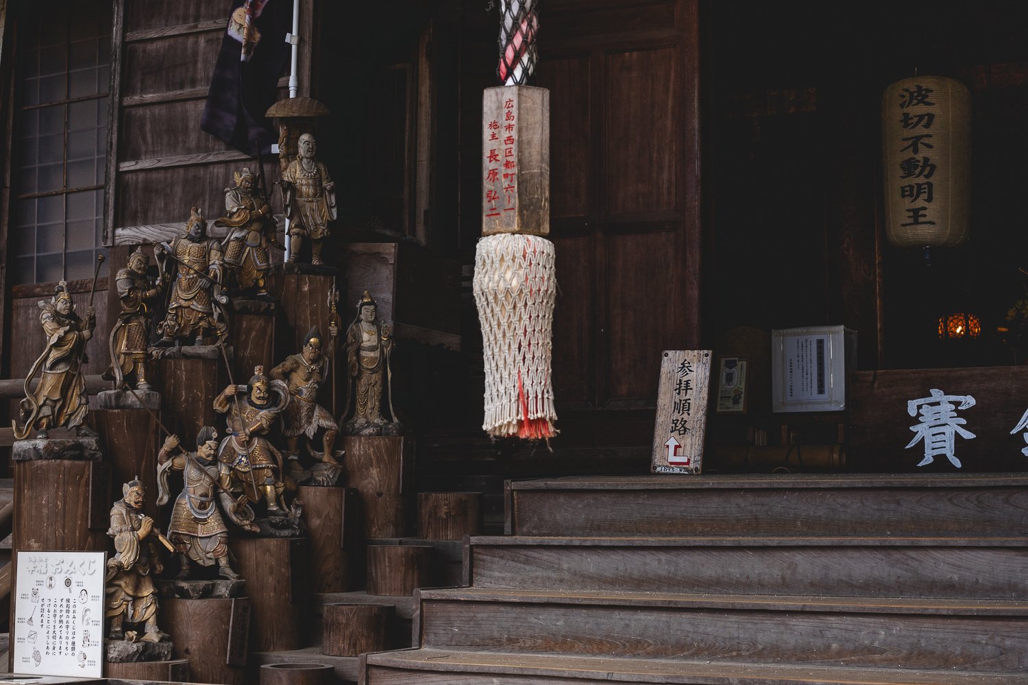 L'entrée d'un des bâtiments du temple :  un escalier de bois semblent gardé par une série de petites statues de bois posées à côté. En haut des marches se trouve une énorme corde tressée suspendue.