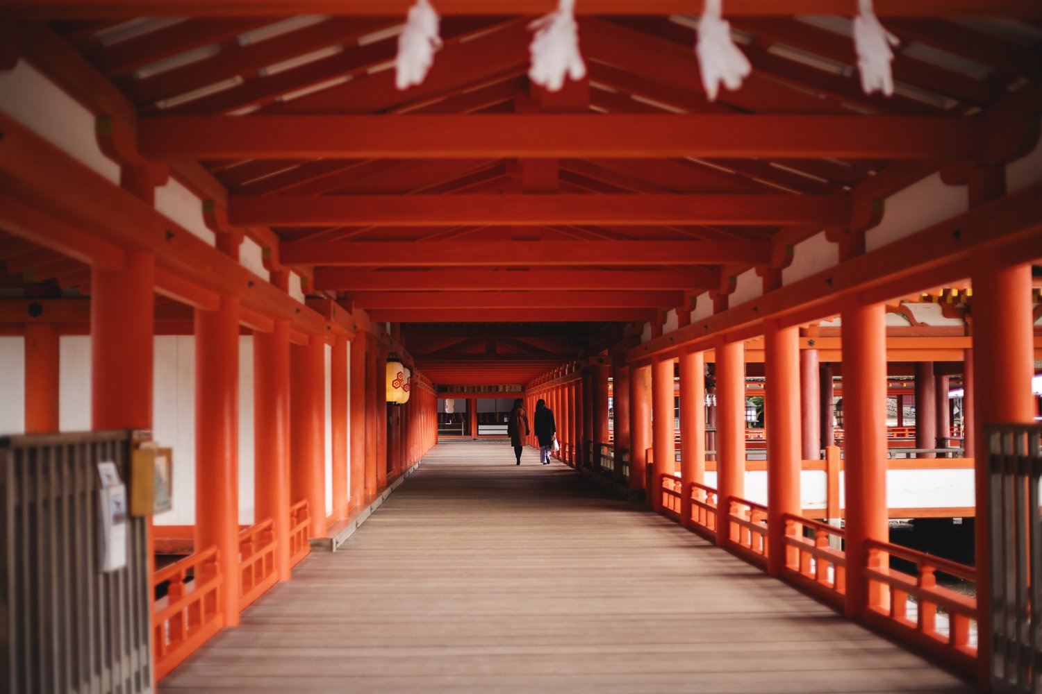 Un couloir dans le sanctuaire Itsukushima à Miyajima. Une allée de bois est entourée de poutres vermillons de chaque côté et au plafond.