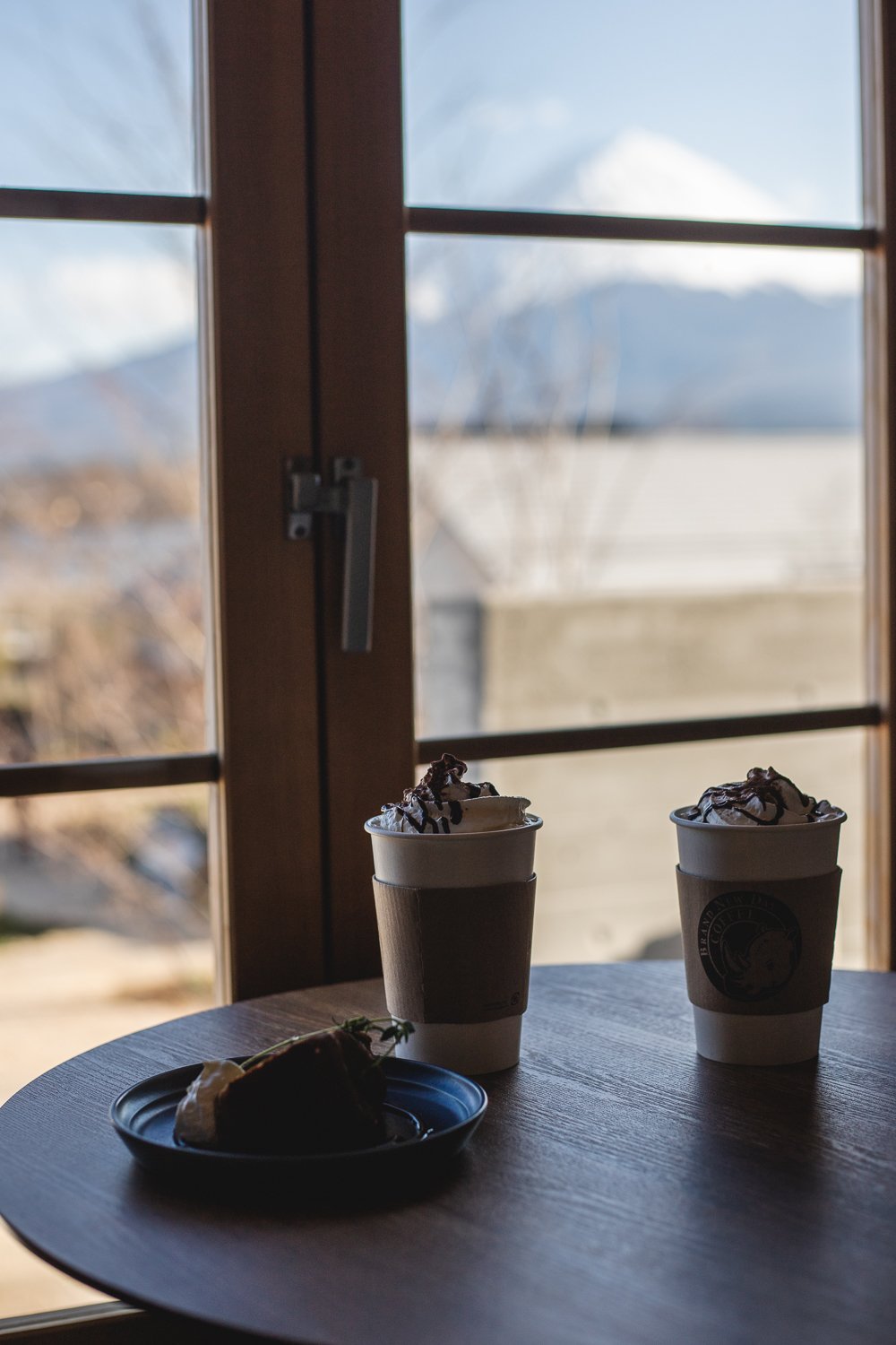 deux chocolats chaud sur une table devant une fenêtre à travers laquelle on aperçoit le Mont Fuji