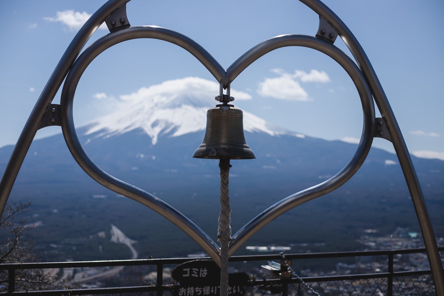 Un cloche est fixée dans une structure en forme de cœur. On peut voir le mont Fuji au loin.