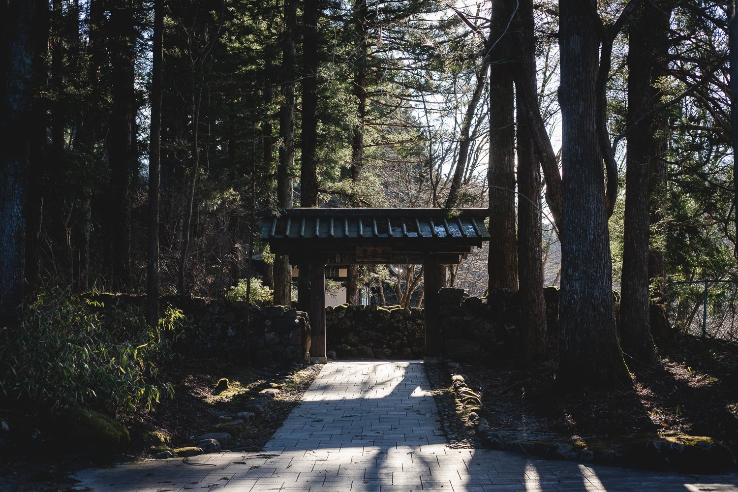Un chemin pavé mène vers un portal en bois au milieu des arbres.