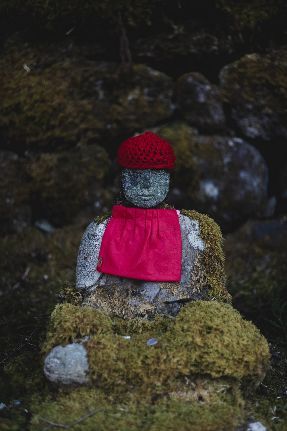 Une statue de bouddha Jizo avec son bonnet de laine rouge et son bavoir assorti.