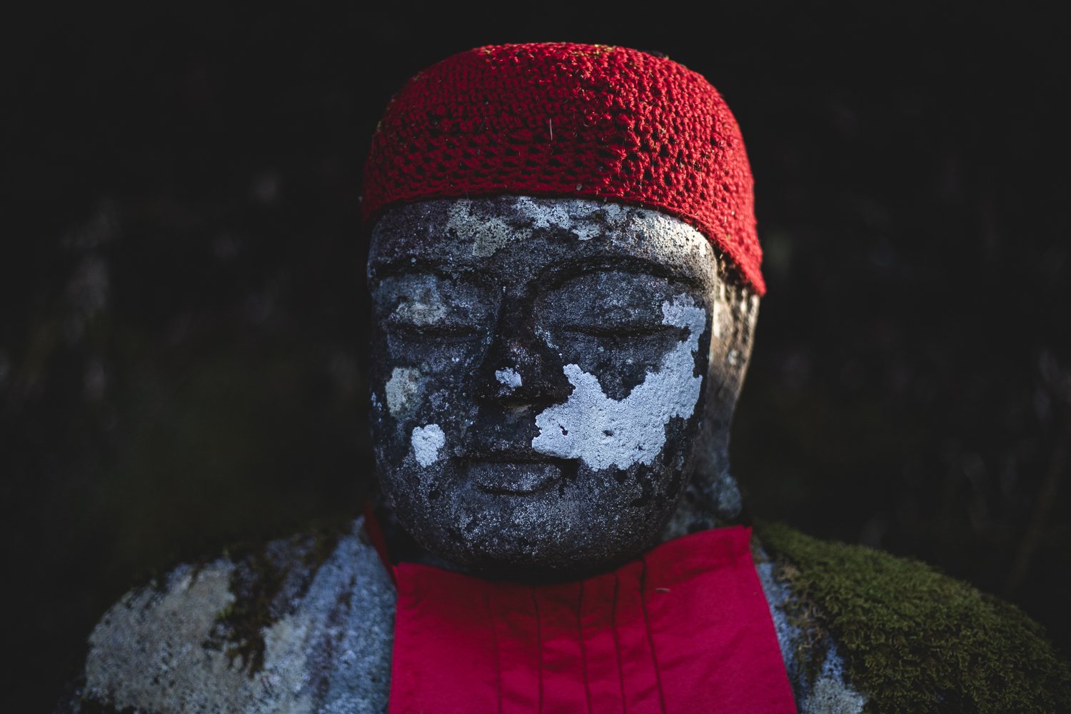 Gros plan sur le visage d'une statue de bouddha Jizo avec son bonnet de laine rouge.