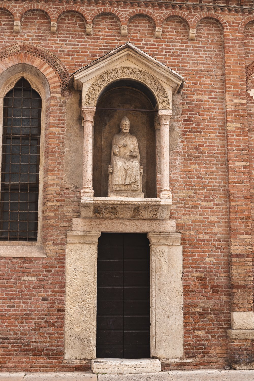 Une porte annexe. La porte est surplombée d'une statue d'un personne ecclésiastique assis