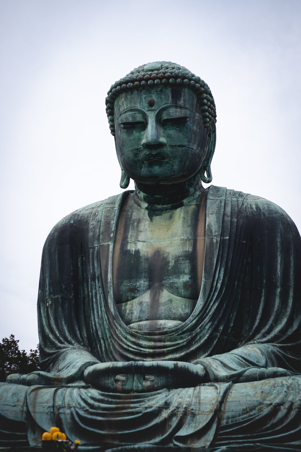 Le grand bouddha de Kamakura en bronze. Il est assis en tailleur et ses mains sont jointes, paumes vers le haut.