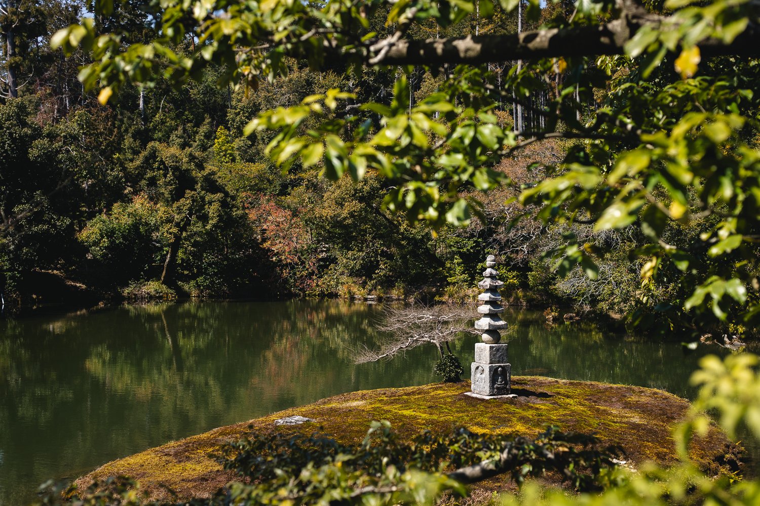 Un étang au temple Kinkaku-ji, au premier plan une petite sculpture qui ressemble à une petite pagode en pierre.