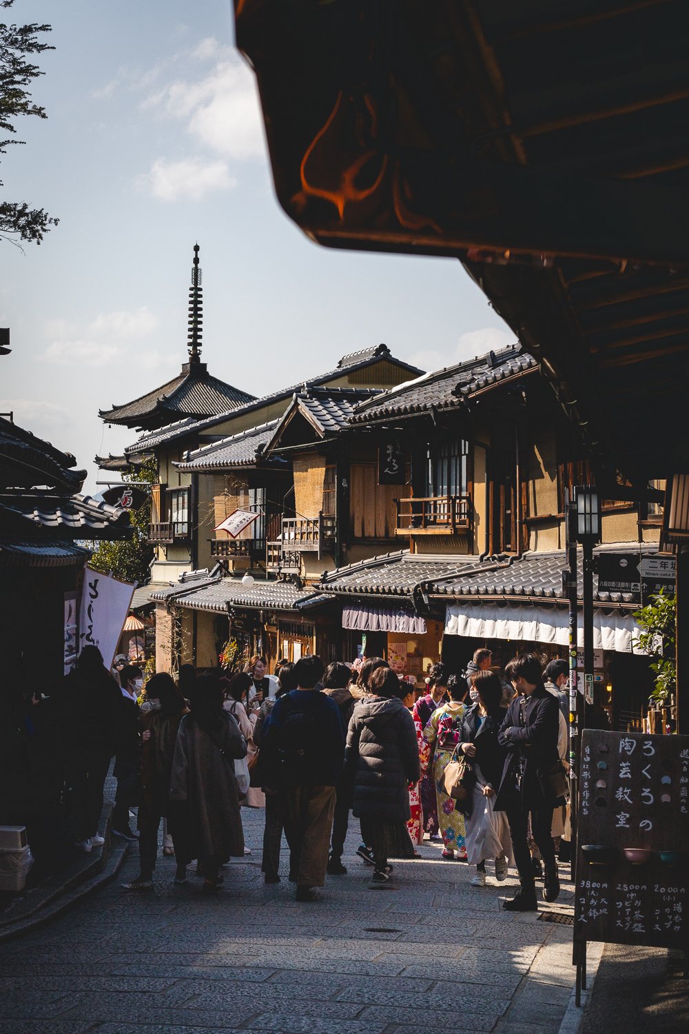 DU monde dans une rue de Kyoto, les façades des maisons sont en bois et on devine une pagode au bout de lar ue