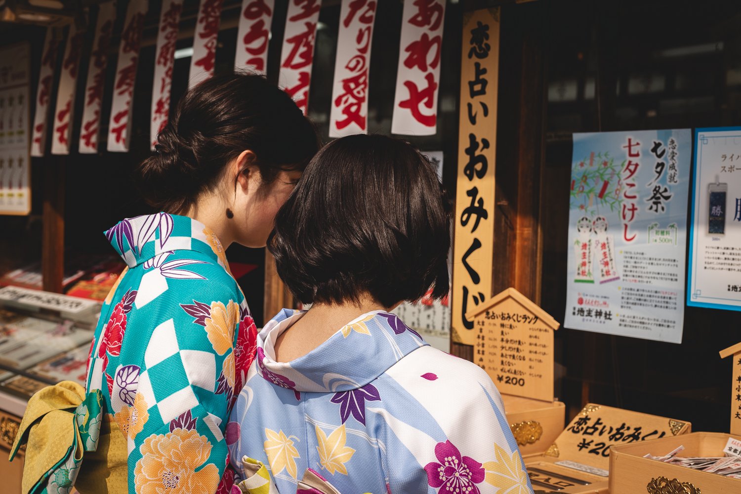 Deux personnes en yukaka de dos qui regardes des objets en vente dans le temple.