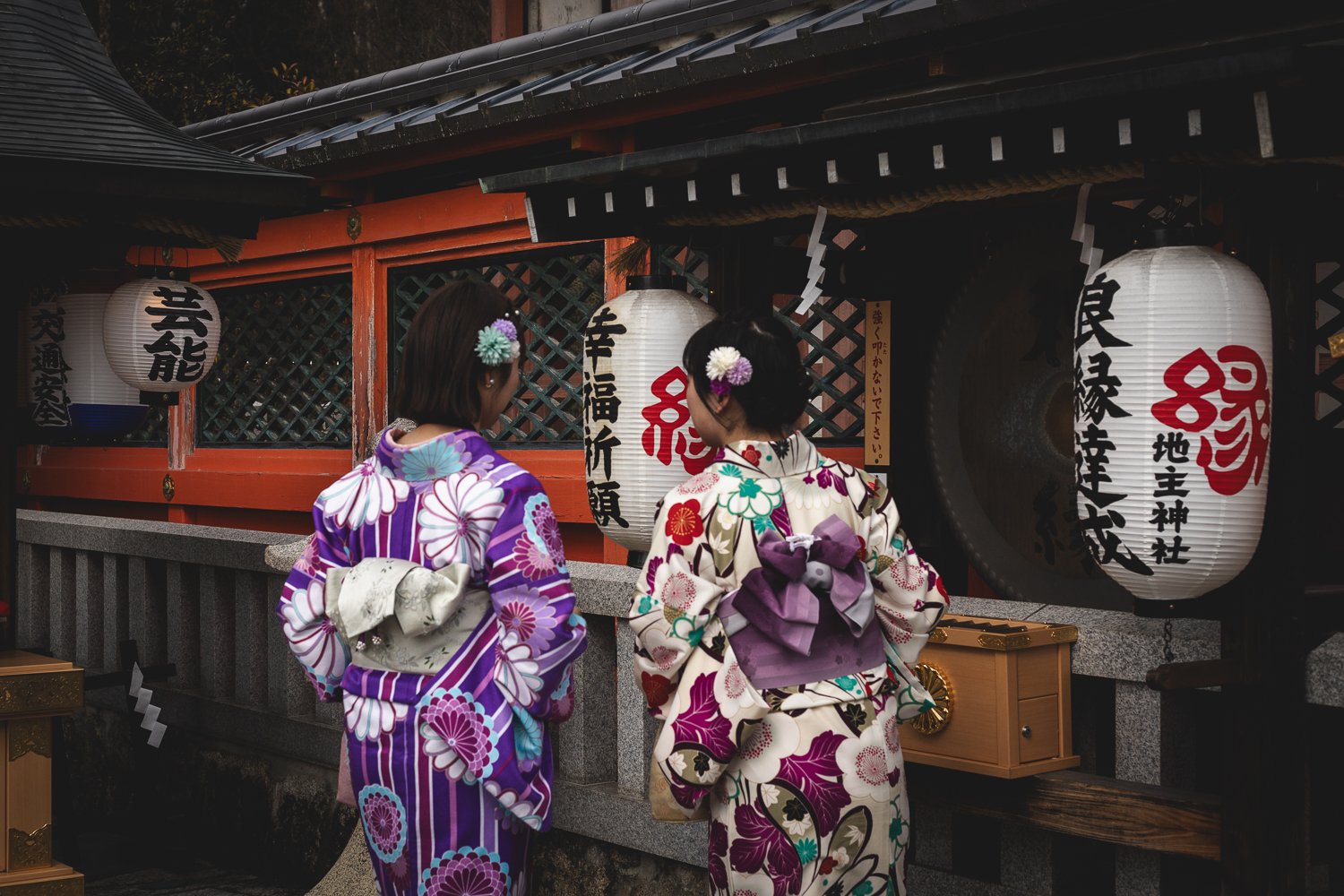 Deux personnes de dos en yukata près d'un bâtiment avec des lanternes de papier